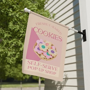 May include: A pink and beige banner with the text "FRESHLY-BAKED COOKIES SELF-SERVE POP UP SHOP". The banner features a basket of colorful flower-shaped cookies.