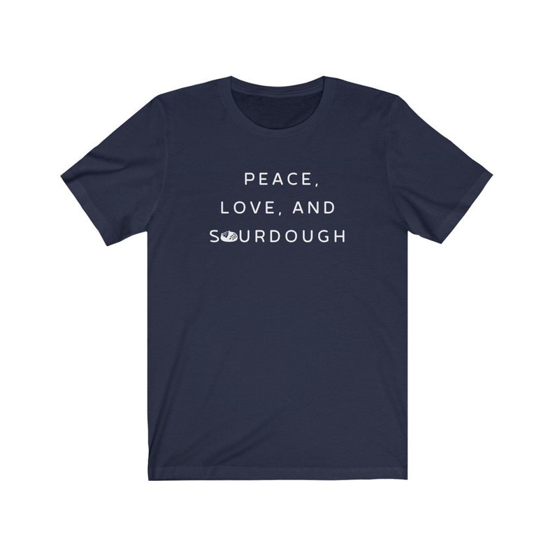 Pode incluir: Uma camiseta azul marinho com o texto "Peace, Love, and Sourdough" impresso em branco na frente.