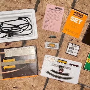 May include: A Märklin mini-club electric train set including a blue power controller in a white styrofoam tray, a cardboard box, a 1979 catalog, a green Ratgeber booklet, an orange Set program, a pink Caution-Electric Toy sheet, and track pieces.