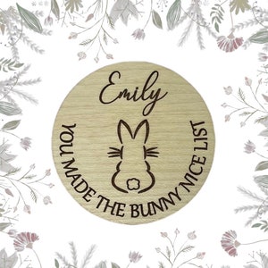 Könnte beinhalten: Ein rundes Holzschild mit dem Text "You made the bunny nice list" und dem Namen "Emily" in Kursivschrift. In der Mitte des Schildes befindet sich eine Hasenillustration.