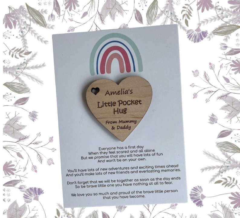 Pu&ograve; includere: Un portafortuna di legno a forma di cuore con il testo "Amelia's Little Pocket Hug" e "From Mummy & Daddy". Il cuore &egrave; attaccato a una carta con un design arcobaleno e un messaggio sulle nuove avventure e l'amicizia.