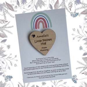 Pu&ograve; includere: Un portafortuna di legno a forma di cuore con il testo "Amelia's Little Pocket Hug From Mummy" su una carta bianca con un'illustrazione di arcobaleno. La carta include una poesia sul primo giorno di un bambino.
