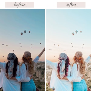 May include: Two people wearing white shirts and patterned head scarves stand with their arms raised in the air, looking at a field of hot air balloons in the sky. The sky is a light blue with a hint of pink in the distance.
