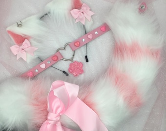 May include: A white and pink cat ear headband, a pink collar with heart and gem accents, and a fluffy tail. The set includes a pink bow and a paw print pendant. The tail has pink stripes.