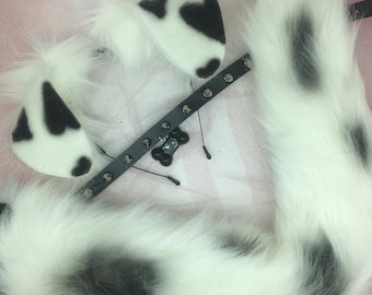 May include: A set of white and black spotted cosplay accessories, including a fluffy tail, ear-shaped headbands, and a studded black collar with a bone charm. The items are designed to resemble a dalmatian.