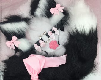 Op de afbeelding: Een set van zwarte en witte nep bontstaarten met roze strikken en een zwarte choker met roze strikken en een pootje bedel.