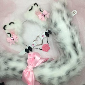 May include: White faux fur tail with black spots, a matching pair of white faux fur cat ears with pink bows, and a black and white choker with a heart charm and pink paw charm.