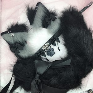 May include: A black faux fur tail with a black satin ribbon bow, a black faux fur choker with a silver paw charm, and two gray faux fur cat ears with black satin ribbon bows.
