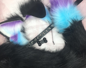 May include: A cosplay set featuring black, purple, and blue faux fur cat ears and tail. The set includes a black leather collar with a bone-shaped charm and a matching tail. The ears have a gradient of purple and blue.