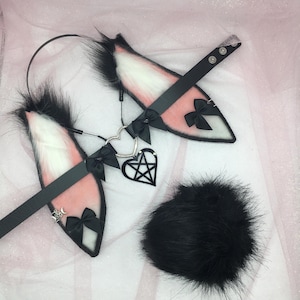 May include: Black and pink faux fur bunny ears headband with a black choker and a pentagram charm. The set also includes a black faux fur tail.