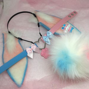 May include: A pastel-colored cosplay set featuring a black headband with attached ears, a pink collar with a paw print, and a fluffy tail. The ears and tail have white, pink, and blue accents, and the set includes satin bows.