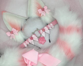 Op de afbeelding: Een wit en roze cosplay set met pluizige kattenoren, een gestreepte staart en een roze choker met een pootafdruk bedel. De oren en staart hebben roze accenten en zijn versierd met roze strikken.