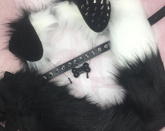 May include: A black and white faux fur cosplay set featuring a tail, ears, and a studded collar with a bone-shaped charm. The ears have silver spikes. The tail is long and fluffy.