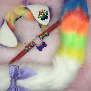 May include: A colorful cosplay set featuring a rainbow-colored faux fur tail, a headband with white ears and a paw print, and a red collar with a heart-shaped charm and a purple bone. The set includes a large purple bow.