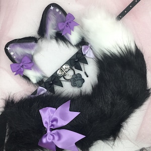 May include: A set of purple and white furry cat ears, a black faux leather collar with a paw charm, and a black and white furry tail with a purple bow.