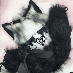 May include: A black faux fur tail with a black satin ribbon bow and a silver charm with a pentagram design. The tail is attached to a black choker with silver charms and a heart-shaped pendant.