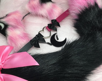 Pode incluir: Um conjunto de orelhas de gato rosa e preto, coleira e cauda. As orelhas são rosa e brancas, a coleira é rosa com laços pretos e um pingente em forma de coração, e a cauda é preta. Para cosplay ou fantasia.