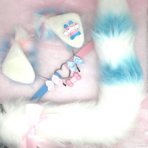 May include: A fluffy white, blue, and pink cosplay set featuring a tail, ears, and a collar. The ears have a paw print design. The collar has a heart and bone charm with bows.