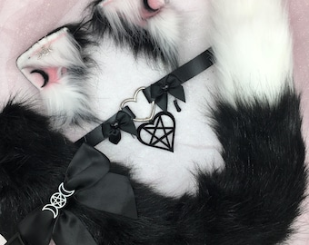 May include: A black and white faux fur cat tail, ears, and choker set. The ears are white with black tips and pink inner ears. The choker features a silver heart and pentagram charm. The tail has a large black bow with a silver moon charm.
