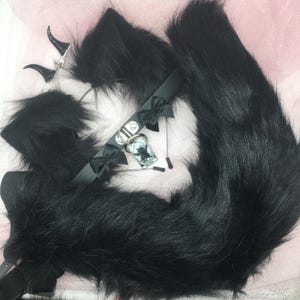 May include: A black cosplay set featuring a fluffy tail, cat ears, and a choker with a pendant. The set includes a pair of clip-on horns. The items are made of faux fur and satin.