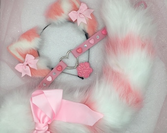 Puede incluir: Un conjunto de diadema, collar y cola de orejas de gato rosa y blanco. Las orejas y la cola son esponjosas, con acentos rosas. El collar es rosa con detalles de corazón y gemas, y un dije de huella de pata. Un gran lazo rosa está unido a la cola.