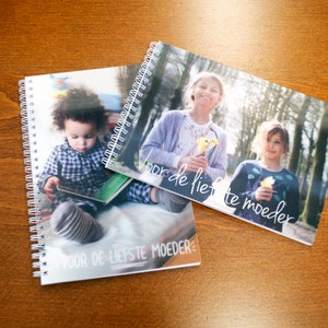 Könnte beinhalten: Zwei spiralgebundene Notizbücher mit bunten Covern, die Fotos von Kindern zeigen. Der Text auf den Covern lautet "voor de liefste moeder", was mit "für die liebste Mutter" übersetzt werden kann.