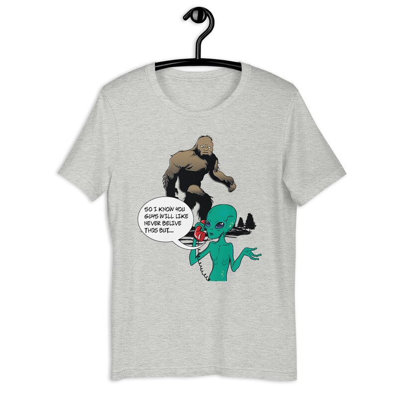 May include: A grey t-shirt with a cartoon image of a green alien on the phone with Bigfoot. The alien is saying "So I know you guys will like never believe this but..."
