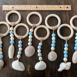 May include: Seven wooden rings with blue and white beads and seashells hanging from them. The rings are strung with twine and the beads are strung on twine. The seashells are different shapes and sizes.