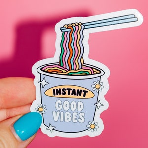 May include: A sticker of a cartoon instant noodle cup with rainbow noodles and chopsticks. The cup says "Instant Good Vibes".