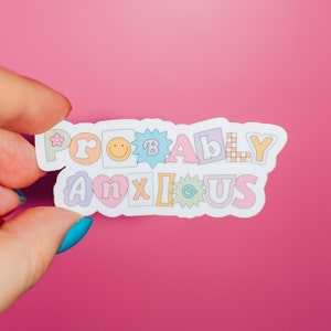May include: A white sticker with the text "Probably Anxious" in colorful, outlined letters. The letters are in different shapes and sizes, with some featuring small decorative elements.