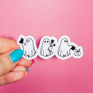 May include: Four white ghost stickers on a pink background. The ghosts are in a line and each one is doing a different activity. The first ghost is holding a butterfly, the second ghost is holding a flower, the third ghost is holding a watering can, and the fourth ghost is watering a pumpkin.
