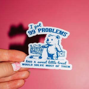 May include: A white sticker with blue text and a cartoon bear pushing a shopping cart. The text reads "I got 99 problems and a sweet little treat would solve most of them."