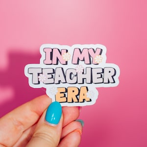 May include: White sticker with pink, grey, and orange lettering that reads "In My Teacher Era" with small white flowers around the text.