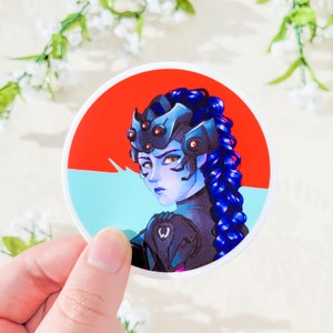 May include: A round sticker featuring a blue-haired character with a red and blue background. The character has a black and white suit with a spider-like design on their head.