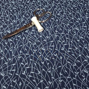 May include: Navy blue fabric with a white leaf and stem pattern. A pair of silver scissors and a spool of white thread are on top of the fabric. The scissors are open, ready for cutting.