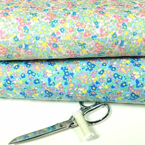 May include: Two rolls of floral fabric in pastel shades, with tiny blue, yellow, and pink flowers on light blue and pink backgrounds. A pair of scissors and a spool of thread are in the foreground, suggesting sewing or crafting.