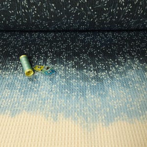 May include: Fabric with a dark blue floral pattern fading to light blue and cream. White leaf-like designs are scattered across the material. A spool of green thread and two sewing clips are on the fabric.