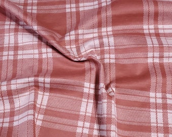 May include: Close-up of a fabric with a plaid pattern. The fabric has a reddish-brown background with a white grid pattern. The fabric is folded and draped, creating shadows and texture.