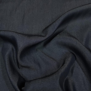 May include: A solid dark charcoal gray fabric with a smooth, slightly lustrous finish. The material is draped in soft, flowing folds, creating deep shadows and subtle highlights across the surface that emphasize its fine, uniform texture.
