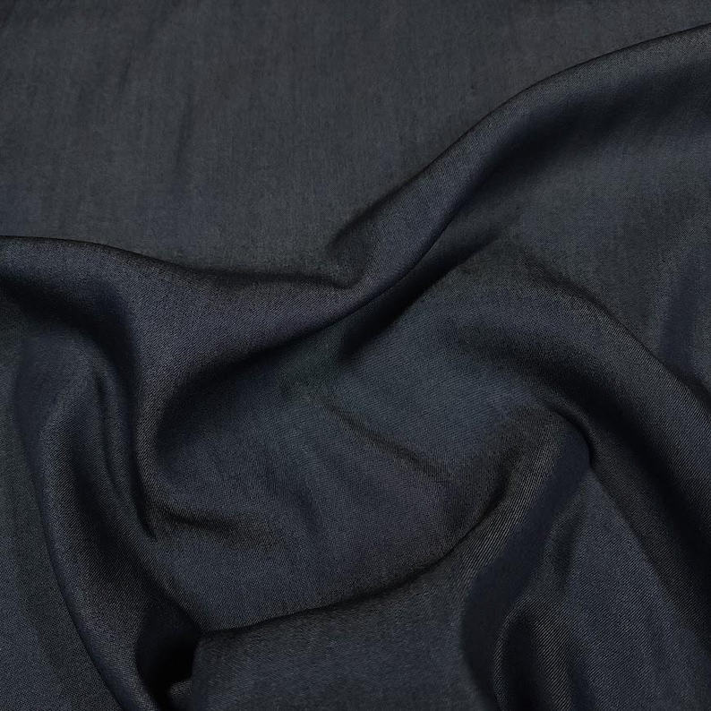 May include: A solid dark charcoal gray fabric with a smooth, slightly lustrous finish. The material is draped in soft, flowing folds, creating deep shadows and subtle highlights across the surface that emphasize its fine, uniform texture.