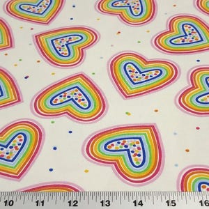 K&ouml;nnte beinhalten: Wei&szlig;er Stoff mit einem sich wiederholenden Muster aus regenbogenfarbenen Herzen. Jedes Herz ist rosa umrandet und mit Schichten aus Gelb, Orange, Gr&uuml;n und Blau gef&uuml;llt. Kleine, bunte Punkte sind &uuml;ber den Hintergrund verstreut.