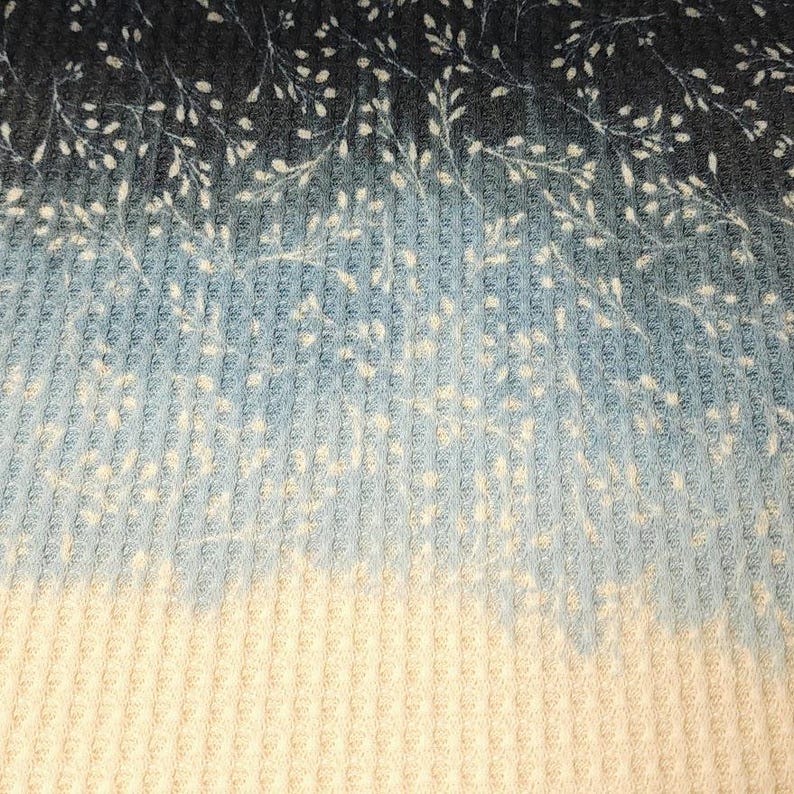 May include: Textured fabric close-up with a gradient design. The top section is dark blue, fading to light blue, and then to cream at the bottom. Small white floral patterns are scattered across the dark blue area of the fabric.