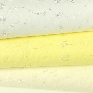 May include: Close-up of three layers of fabric in shades of white and yellow. The fabric is embroidered with delicate floral and leaf patterns in a lighter color. The layers are stacked, showcasing the texture and design of the material.