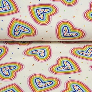 K&ouml;nnte beinhalten: Wei&szlig;er Stoff mit einem sich wiederholenden Muster aus regenbogenfarbenen Herzen. Jedes Herz ist rosa umrandet und mit konzentrischen Regenbogenstreifen gef&uuml;llt. Kleine, bunte Punkte sind &uuml;ber den Hintergrund verstreut.