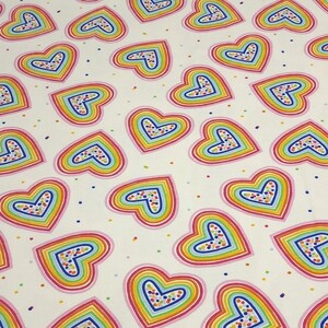 K&ouml;nnte beinhalten: Wei&szlig;er Stoff mit einem sich wiederholenden Muster aus regenbogenfarbenen Herzen. Jedes Herz hat einen mehrfarbigen Umriss und eine gesprenkelte Mitte. Kleine, bunte Punkte sind &uuml;ber den Hintergrund verstreut.