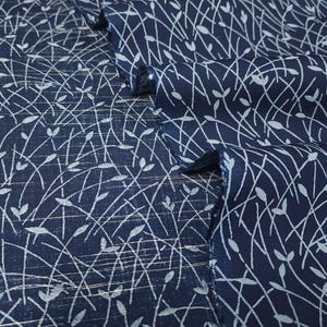 May include: Close-up of navy blue fabric with a white, delicate, linear pattern. The design features thin, curved lines and small leaf-like shapes, creating a textured, organic aesthetic. The fabric is folded, showing the pattern's repeating nature.