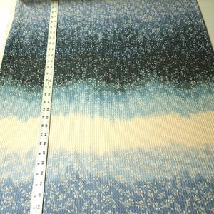 May include: Blue and white fabric with a gradient design. The fabric has a ribbed texture and a pattern of small white floral sprigs. A ruler is placed vertically along the fabric, showing measurements in inches.