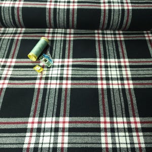 May include: Black and white plaid fabric with red accent stripes. A spool of green thread, a blue clip, and two yellow clips are on the fabric. The fabric is rolled up in the background.