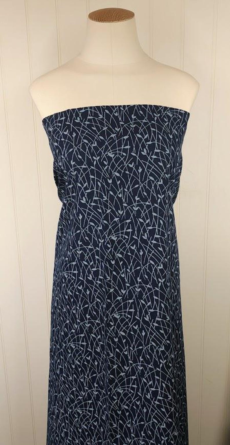 May include: A navy blue fabric draped over a mannequin. The fabric features a delicate, light blue pattern of curved lines and small leaf-like shapes. The fabric is likely used for clothing or home decor.