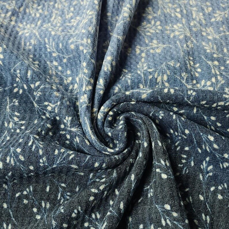 May include: Close-up of blue fabric with a floral design. The fabric has a waffle texture and a gradient effect, changing from light to dark blue. White floral sprigs are scattered across the surface.